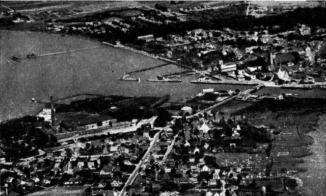 (Foto). Gammel købstad med ny forstad. Hinsides havneløbet (på tværs af billedet) det gamle Stege med kirken, afgrænset mod land af den træbevoksede voldlinie. I forgrunden forstaden Lendemarke opvokset om sukkerfabrikken (til venstre, grl. 1883–84) o.a. industrianlæg og langs købstadens vejforbindelse til Kalvehave og Vestmøn.Luftfoto Nowico.