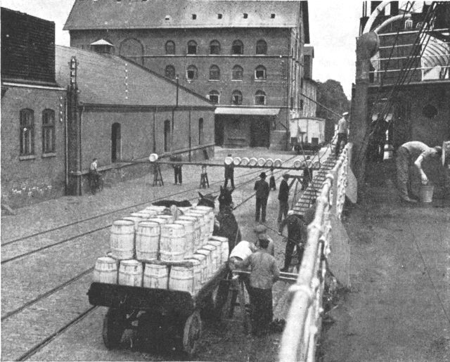 (Foto). Lastning af smør til eksport i Odense havn. I havnebyerne bidrager søhandelens pakhuse, siloer og kølehuse til at præge bybilledet.Fot. Jonals.