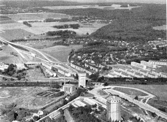 (Foto). Udsigt over Jægersborg station mod nordøst. Tværs over forgrunden Nordbanen med Jægersborg S-banestation (bag vandtårnet i billedets midte) ved viadukten over Hørsholmvejen. Denne 1955 åbnede motorvej fører fra billedets nederste højre hjørne skråt op mod venstre; man ser udfletning af sideveje fra motorvejen og veje, der føres over den på vejbroer. Omkring stationen høj boligbebyggelse, længere borte villabebyggelse. Motorvejen, der er façadeløs, drager ingen bebyggelse med sig. I baggrunden Ermelunden og Dyrehaven med Eremitagesletten.
