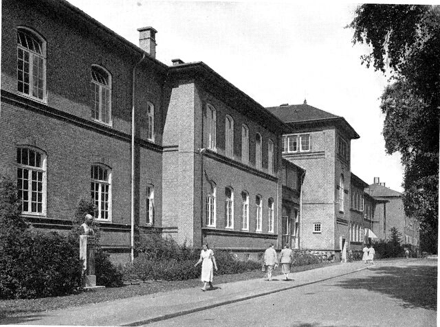 (Foto). Fra Frederiksberg hospital. I forgrunden en af de oprindelige bygninger (nu afdeling for kvindesygdomme), helt tilbage en nyere bygning (bl. a. kirurgisk afdeling). Til venstre buste af overkirurg Ludvig Kraft (udført af Anne Marie Carl Nielsen).