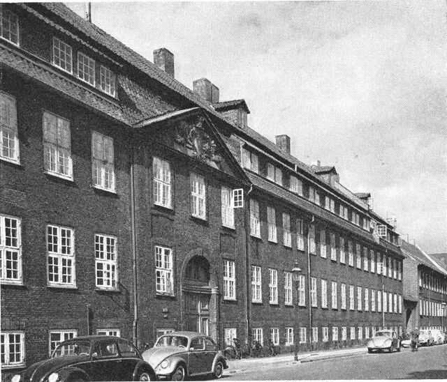 (Foto). En del af Rigensgades kaserne med porten Rigensgade 9. I trekantgavlen derover Christian VII’s monogram. Længst til højre det tidl. munderingsdepot.