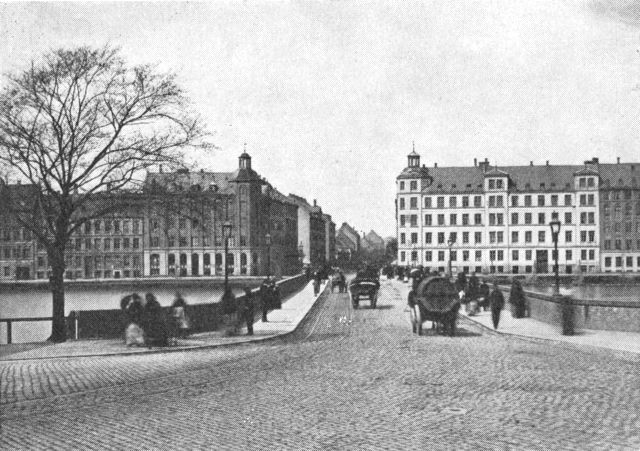 (Foto). Indkørslen til Nørrebro. Fotografi 1865. I forgrunden den ældste dronning Louises bro. Bagved Nørrebrogades nyopførte huse med karakteristiske korresponderende hjørnetårne og længere ude af gaden mere tilfældig bebyggelse.