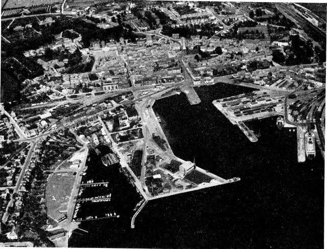 (Foto). Nyborg set fra luften fra sydvest. Omkring den gamle bykerne ses de trækransede rester af den gamle befæstning. Fra havnen fører (omtrent midt i billedet) hovedvej 1 gennem byens centrum for derefter (nærmere billedets overkant) at svinge til venstre mod Odense. I forgrunden t.v. både- og fiskerihavn, i midten Vester- og Østerhavnen og t.h. en del af færgehavnen.