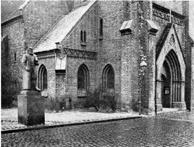 (Foto). Det nordvestre hjørne af kirken, set fra Kirketorvet. Til venstre statue i granit af Anders Sørensen Vedel.