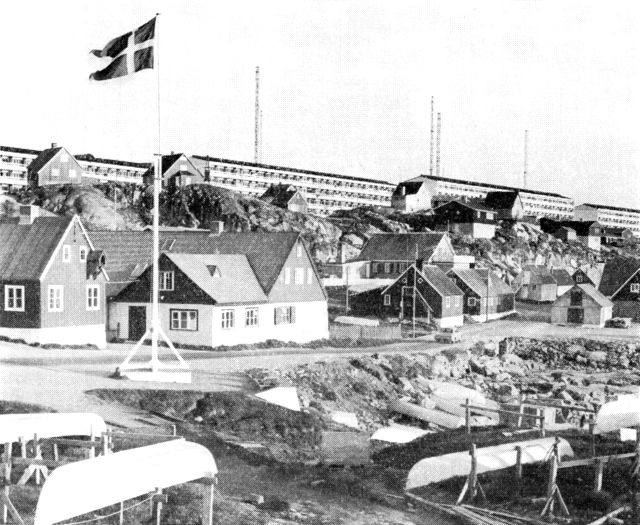 (Foto). Det nye Godthåb vokser op på højene bag den gamle bydel. I forgrunden med flagstangen Hans Egedes første hus i Godthåb, bygget 1728. (F.: Chr. Vibe, 1969).
